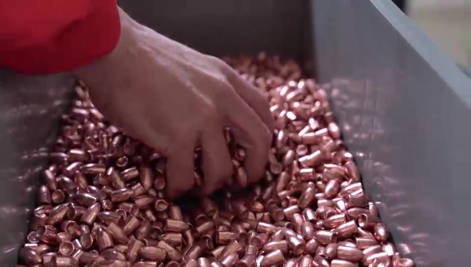 A hand turning over finished copper-plated 9mm projectiles in a steel tray