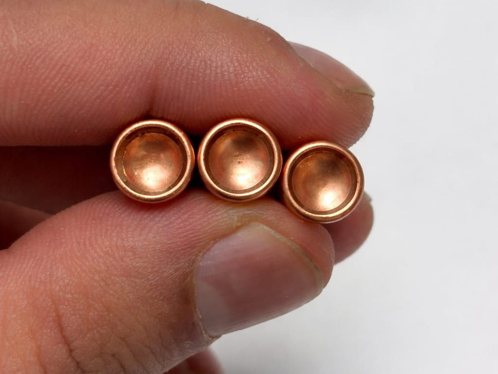 Three TOR44 9mm projectiles held base-up, showing the copper-plated concave base